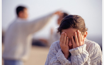 Photo of boy covering his eyes with his hands with two people in the background.