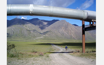 Photo of Andrew Jacobson and colleague hiking along a road with Alaskan pipeline in foreground.