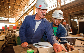 A mentor shows a student apprentice how to measure precision machining angles