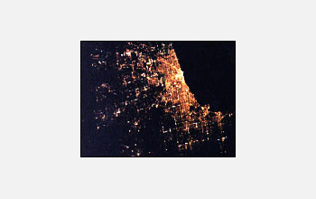 Photo showing bright lights of Chicago on the right fading into dark rural landscapes on the left.