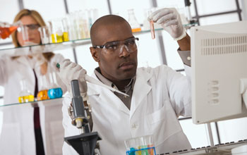 Photo of a male scientist in foreground holding test tube and pipette, female researcher in back.