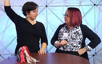 Show hosts Jordan and Charlie side-by-side with paper streamers tied to small fan on a table