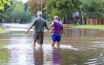 Two men walk hand in hand through a flood-covered street.