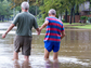 Two men walk hand in hand through a flood-covered street.