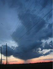 Photo of telephone poles in the foreground with dark clouds in the sky.
