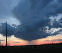 Photo of telephone poles in the foreground with dark clouds in the sky.