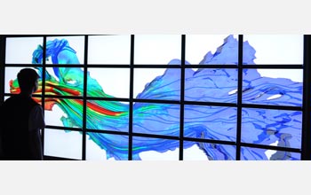 A young man stands in front a bank of computer monitors that project a simulation of river currents.