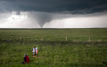 Researchers in the field studying a tornado in the distance.