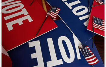 Photo of a pile of red and blue VOTE signs.