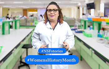 A woman wearing a lab coat in a science lab facing the camera with text #NSFSories and #WomensHistoryMonth