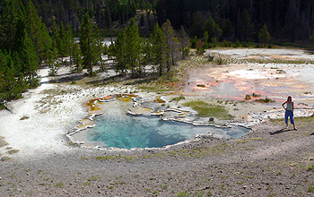 Photo of a woman standing near a hot spring with trees in background